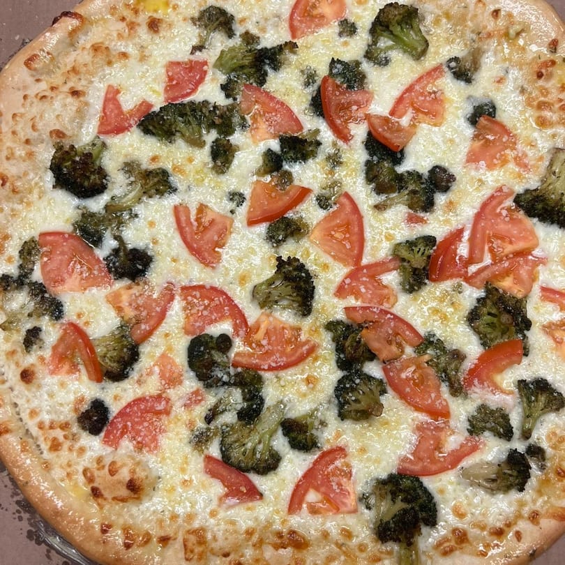 West End Kitchen's white pizza with melted cheese, broccoli florets, and sliced tomatoes.