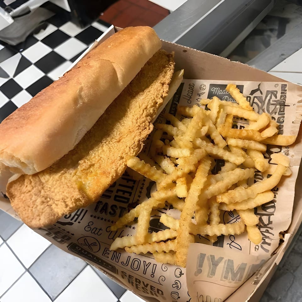 A fried fish sandwich on a bun with a side of crinkle-cut fries in a paper-lined basket.