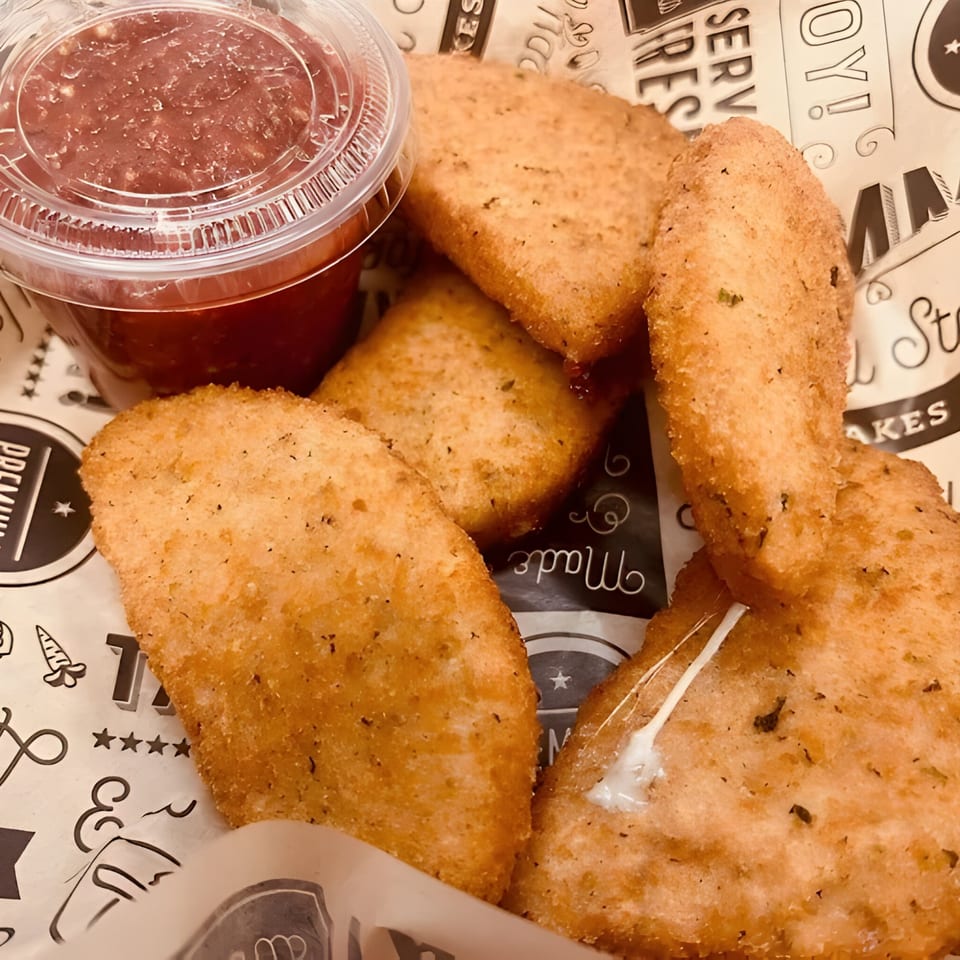 Golden-brown mozzarella sticks with a side of marinara sauce in a plastic cup.